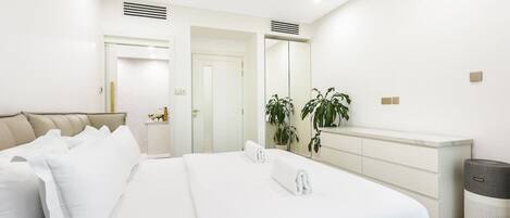 Une chambre à coucher moderne avec un grand lit, une table de chevet, un miroir, une armoire et une poubelle.