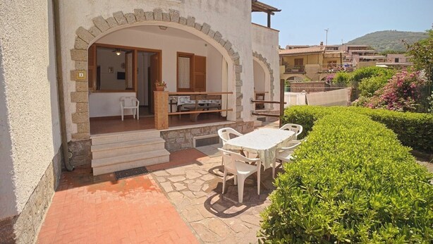 Eine Terrasse mit Tisch und Stühlen, eine Steinsitzbank und ein kleiner Garten mit ordentlich geschnittenen Sträuchern.