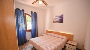 Ein Schlafzimmer mit einem Bett, einem Nachttisch, einem Holz-Kopfteil, einem Deckenventilator und einem Fenster mit Vorhängen.