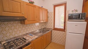 Eine kleine Küche mit Holzausstattung, einem Gasherd, einer Spüle, einer Mikrowelle und einem Kühlschrank.