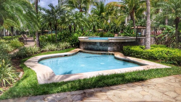 Une piscine rectangulaire bordée de pierres, entourée d’une végétation luxuriante et de palmiers.