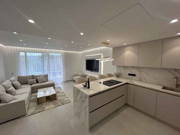 A modern kitchen with a marble countertop, integrated appliances, and a flat-screen TV.