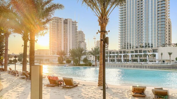 A beachfront hotel with a pool, palm trees, and high-rise buildings in the background.