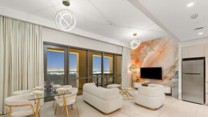 A modern living room with a dining area, a sofa set, a flat-screen TV, and a large window offering a city view.