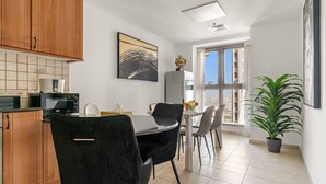 A modern kitchen with wooden cabinets, a dining area with a table and chairs, a large window with a view, and a potted plant.