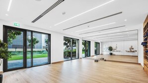 A spacious, modern room with large sliding glass doors leading to a garden, a mirrored wall, and a wooden floor.