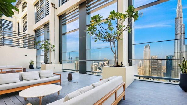 A modern rooftop terrace with seating, large windows, and a view of the city skyline.