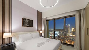 A modern hotel room with a large bed, a nightstand, a wall art piece, and a view of a cityscape through large windows.