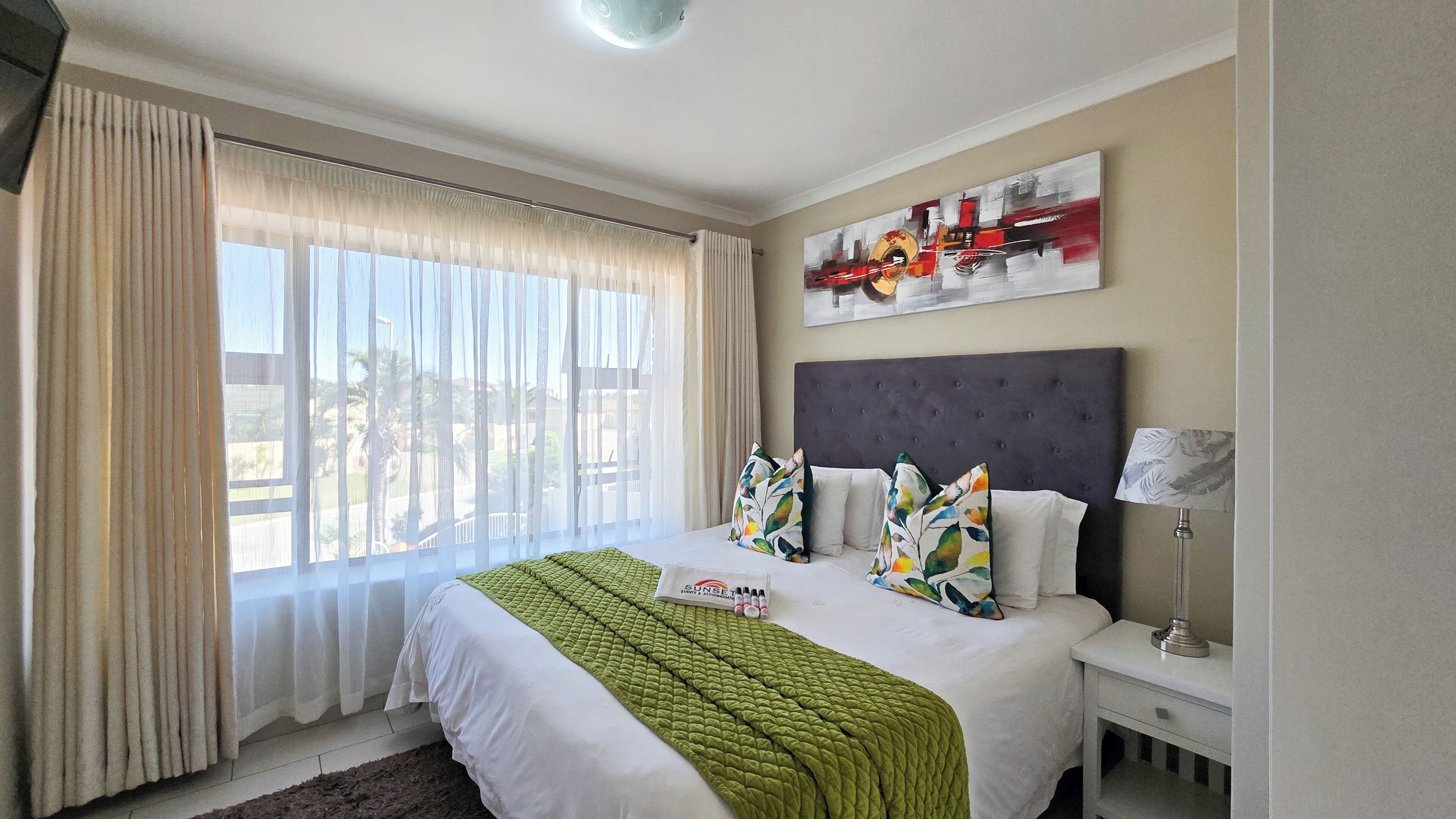 A hotel room with a large bed, a nightstand, a lamp, and a painting on the wall.