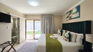 A hotel room with a bed, a TV, a painting, and a view of the outdoors. - Sunset Events and Accommodation  (Gqeberha)
