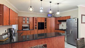 A kitchen with wooden cabinets, a stainless steel refrigerator, a microwave, and a gas stove. - Sunset Events and Accommodation  (Gqeberha)