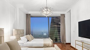 A modern hotel room with a large bed, a TV, and a city view. - Burj Khalifa View | 4BR Home | Walk to Dubai Mall | Pool & Parking (Downtown)