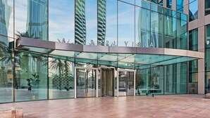 A modern building with a glass facade and a revolving door entrance. - Burj Khalifa View | 4BR Home | Walk to Dubai Mall | Pool & Parking (Downtown)