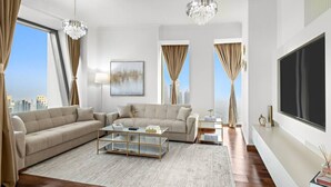 A modern living room with a large sofa, a coffee table, and a TV. - Burj Khalifa View | 4BR Home | Walk to Dubai Mall | Pool & Parking (Downtown)