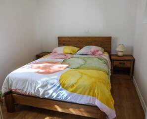 A bed with a colorful quilt, a wooden headboard, a bedside lamp, and a nightstand with a drawer.