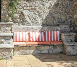 A stone bench with red and white cushions against a stone wall.