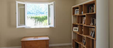 Une pièce avec un banc en bois, une bibliothèque et une fenêtre donnant sur un paysage verdoyant.