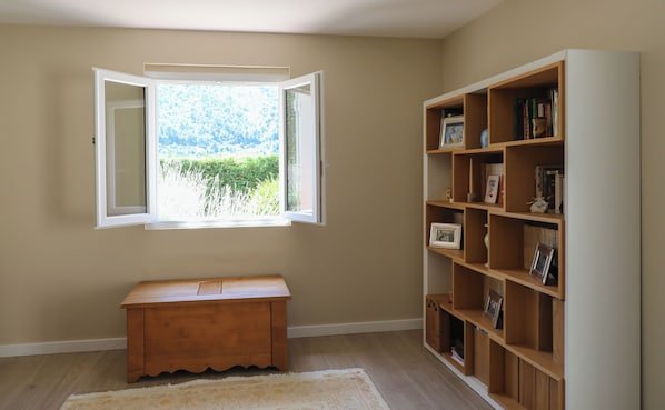 A room with a wooden bench, a bookshelf, and a window with an open view of greenery.