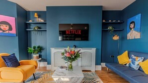 Een moderne woonkamer met een blauwe muur, een Netflix-bord, een bank, een salontafel en decoratieve planten.
