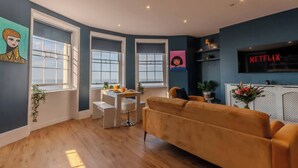Een moderne woonkamer met een bank, een eettafel en een aan de muur bevestigde televisie.