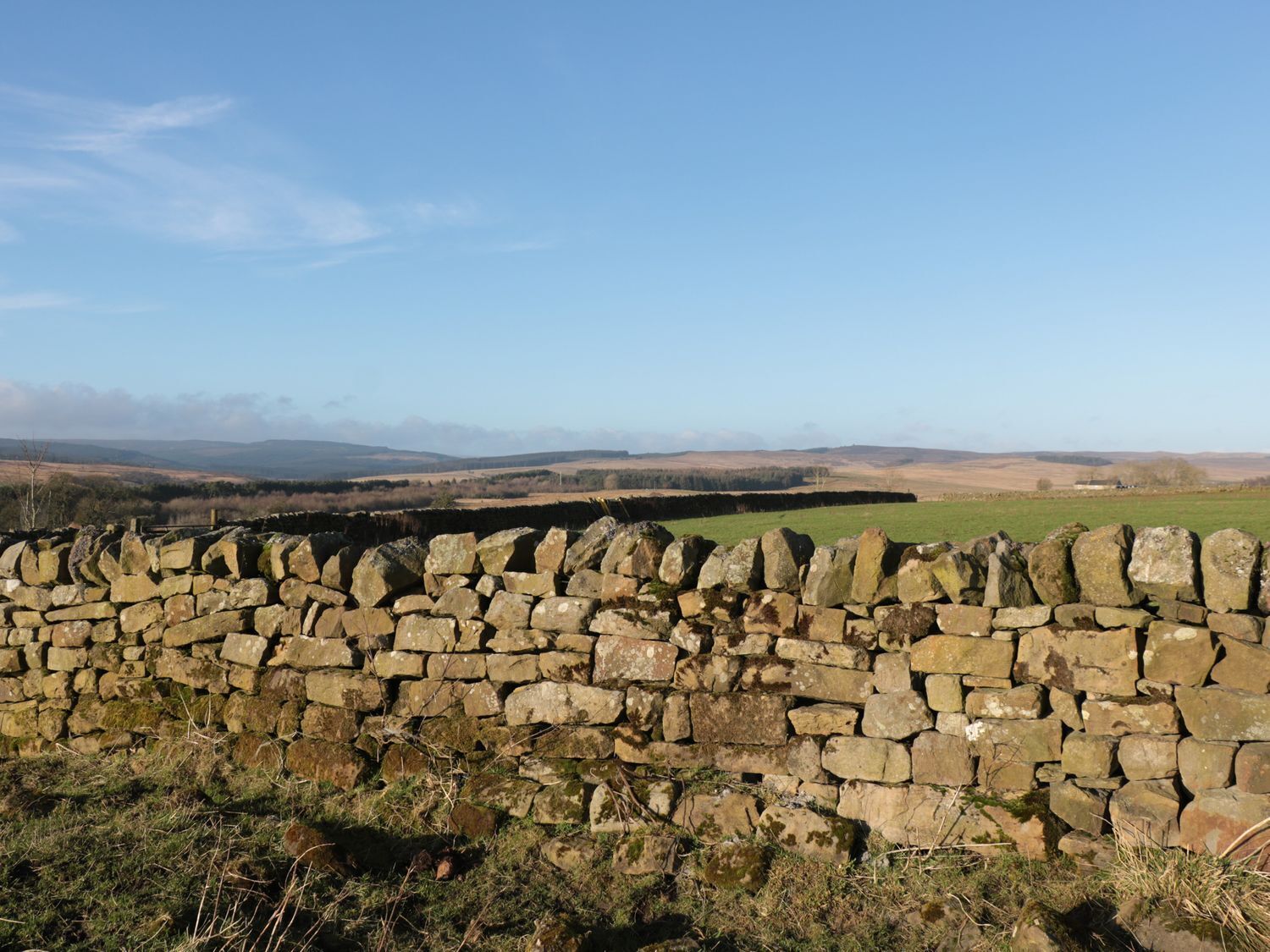 A stone wall with a view of rolling hills and a clear sky.