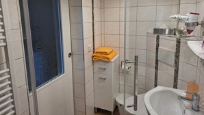 Ett modernt badrum med en duschavdelning i glas, en vit tvättställ och ett litet skåp med en handduk i.