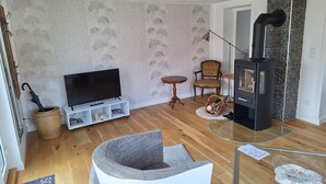 Ett mysigt vardagsrum med en tv, en öppen spis, en korg av rotting och ett litet bord.