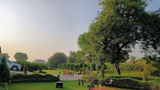 A well-maintained garden with neatly trimmed hedges, a few outdoor tables and chairs, and a parked car. - Rang Vilas (Mathura)