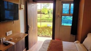 A hotel room with a bed, a TV mounted on the wall, a reception desk, and a view of the outdoors. - Rang Vilas (Mathura)