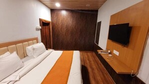 A hotel room with a bed, a television mounted on the wall, and a wooden floor. - Rang Vilas (Mathura)