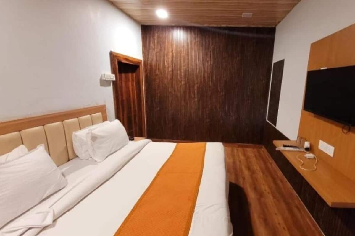 A hotel room with a bed, a television mounted on the wall, and a wooden floor.