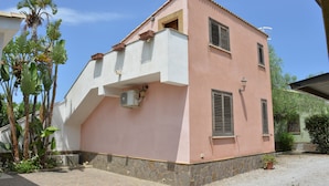A two-story house with a pink facade, stone base, and a small balcony.