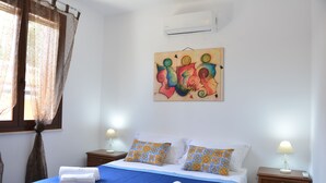 A neatly made bed with blue bedding and decorative pillows, a bedside table with a lamp, and a wall-mounted air conditioner.