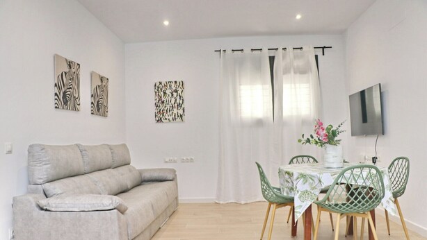 A modern living room with a grey sofa, a dining table with green chairs, and artwork on the walls.