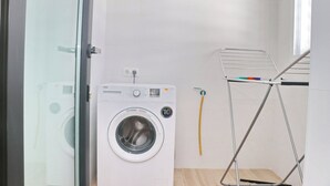 A compact laundry room with a front-loading washing machine, a drying rack, and a small window.