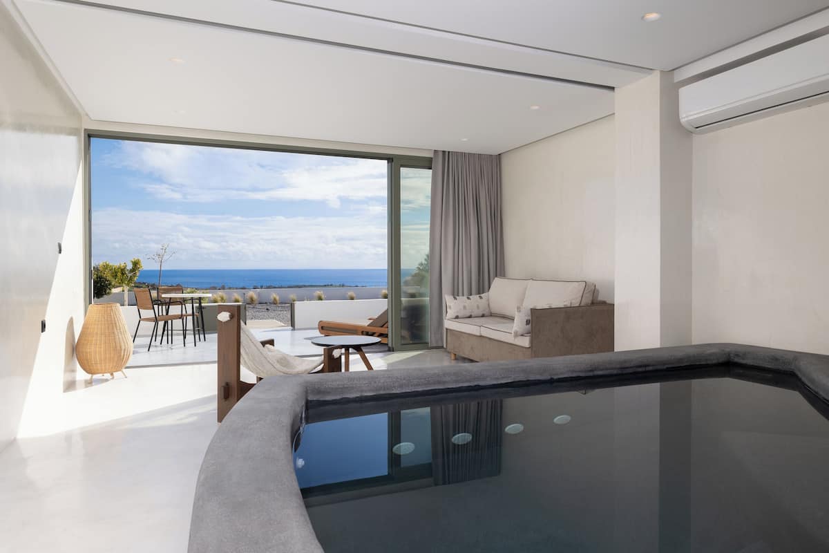 A modern living room with a glass-enclosed balcony, a sofa, a coffee table, and a hot tub.
