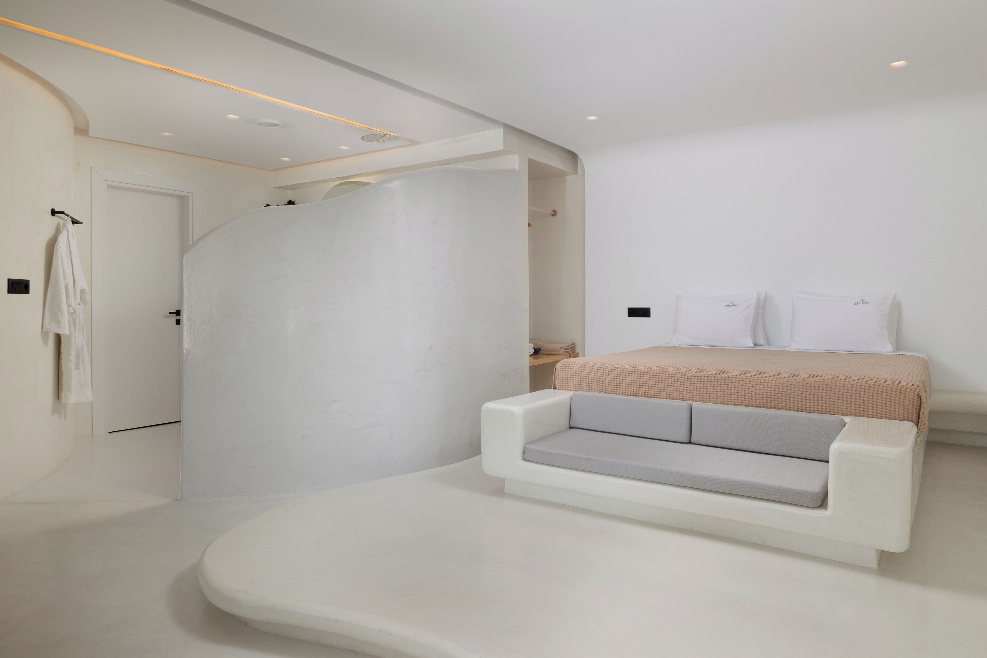 A modern bedroom with a built-in sofa, a bed with white linens, and a white door.