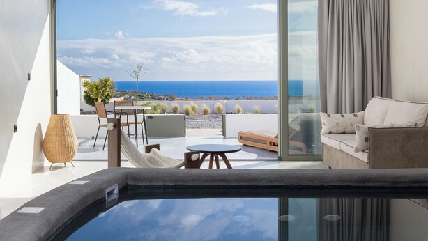 A modern room with a glass-enclosed hot tub, a sofa, and a table with chairs. - Acro Caldo Suites (Akrotiri)
