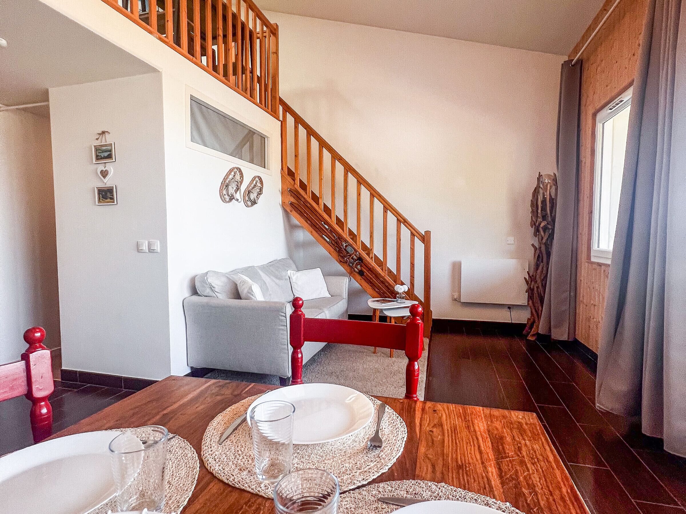 Un coin repas avec une table en bois dressée pour deux personnes, un escalier et un salon agrémenté d’un canapé et d’œuvres d’art décoratives au mur.
