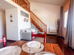 A dining area with a wooden table set for two, a staircase, and a living room with a sofa and decorative wall art.