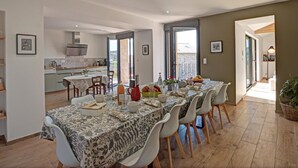 Un vaste espace dédié à la salle à manger, avec une longue table dressée pour six personnes, une cuisine en arrière-plan et un balcon offrant une vue agréable.