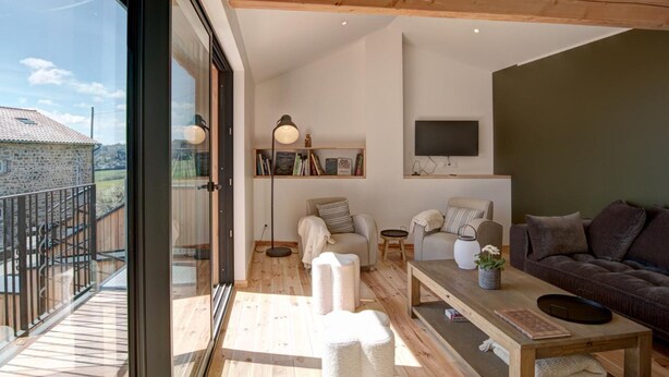 Un vaste espace de vie doté d’un plafond en bois, d’une grande fenêtre et d’un balcon.