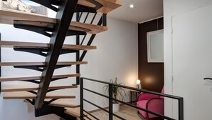 Un intérieur moderne avec un escalier en colimaçon, un fauteuil rose et une plante en pot.