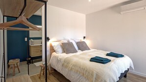 Une chambre à coucher comprenant un lit, des tables de chevet, une armoire suspendue et un petit tabouret.