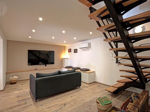 A modern living room with a sofa, a TV, a staircase, and a basket of books.