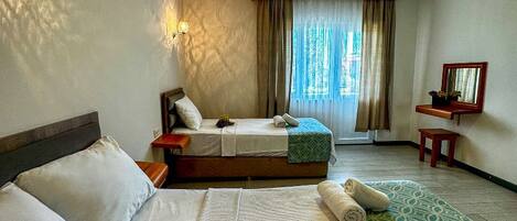 Habitación de hotel con dos camas, un ventanal con cortinas, una mesita con espejo y una lámpara fijada a la pared.