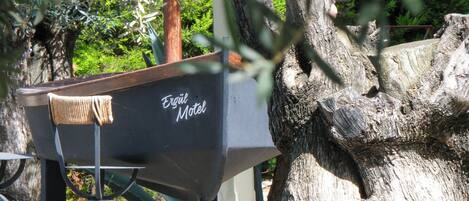Un banco de metal con un letrero que dice 'Ergül Motel' debajo de un árbol.