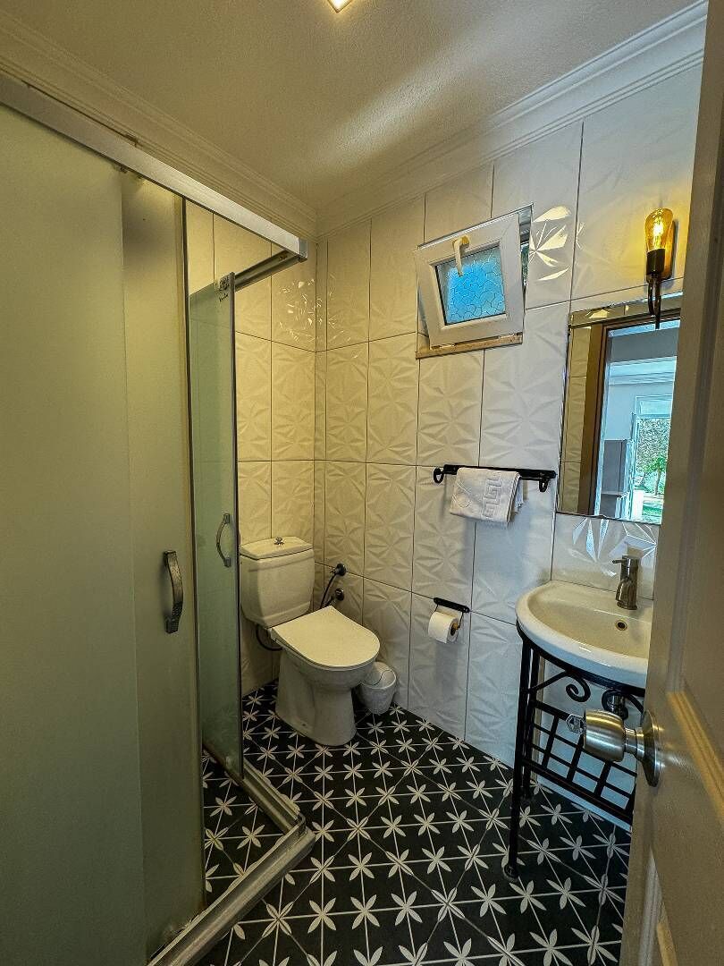 A bathroom with a glass-enclosed shower, a toilet, and a sink with a mirror.