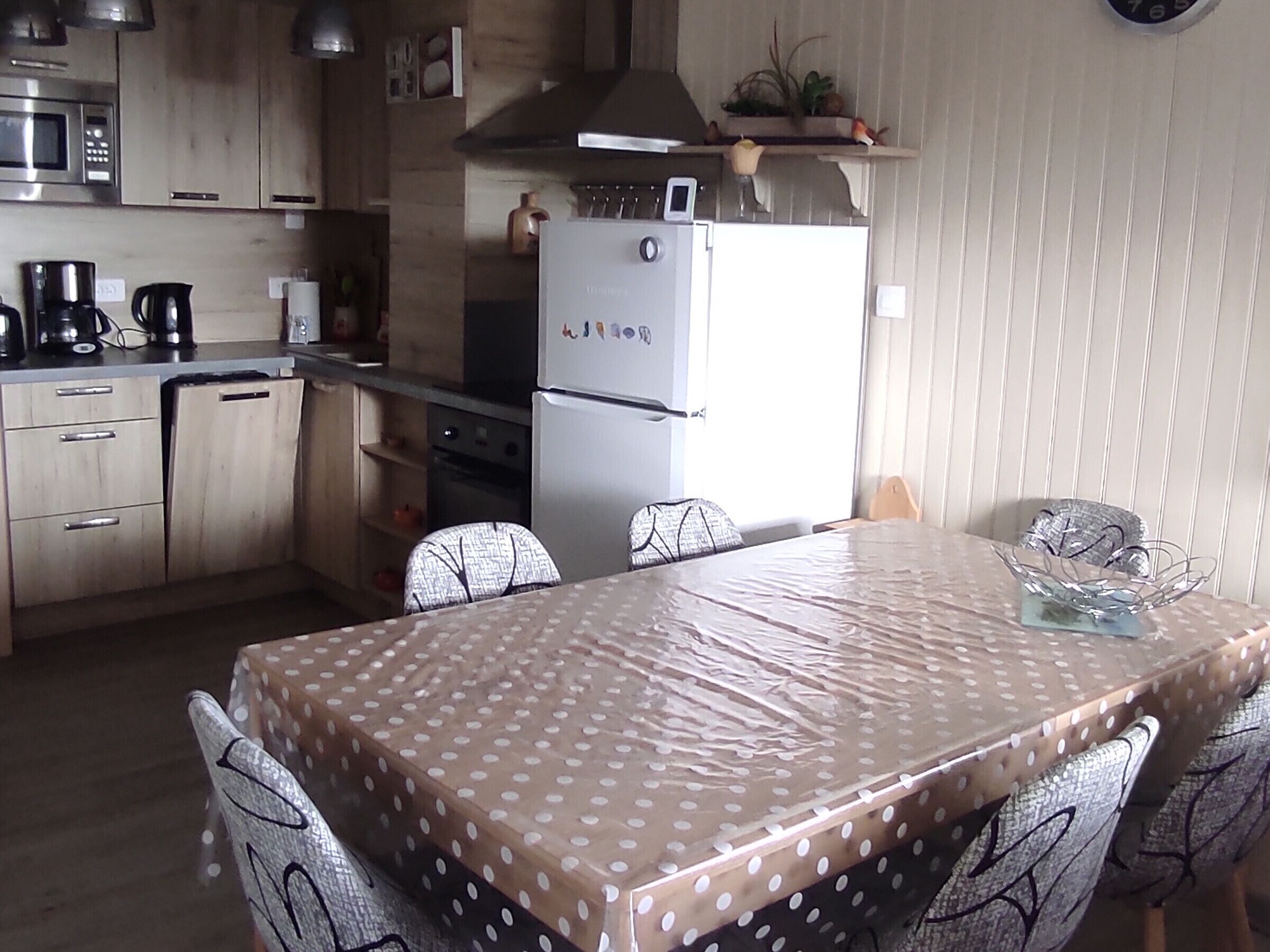 Una cocina equipada con microondas, estufa, refrigerador y una mesa de comedor cubierta con un mantel a lunares.
