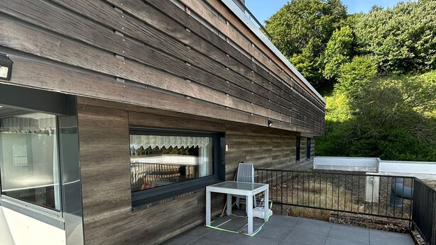 Un edificio moderno con facciata in legno, una porta in vetro e un'area patio con tavolo e sedie.